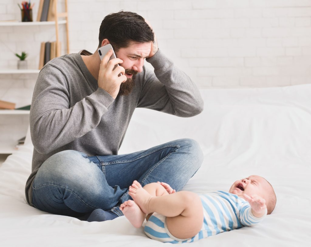 Gestresster Vater am Telefon neben seinem weinenden Baby.