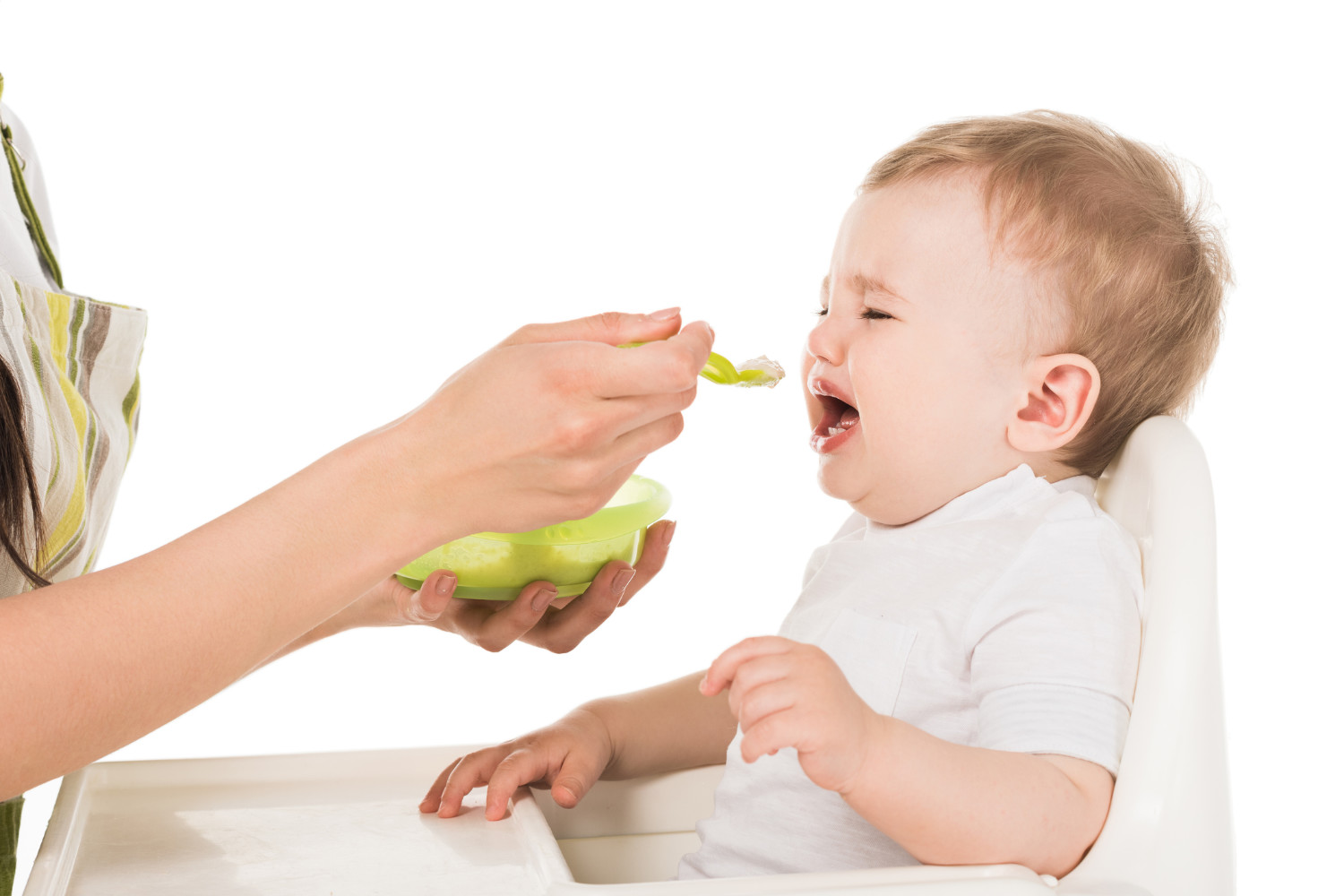Mutter füttert weinendes Baby im Hochstuhl.